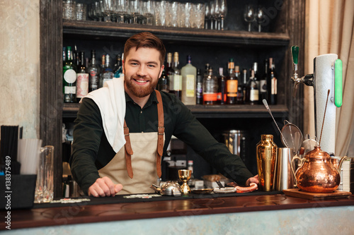 Cheerful young bearded man bartender standing in cafe.