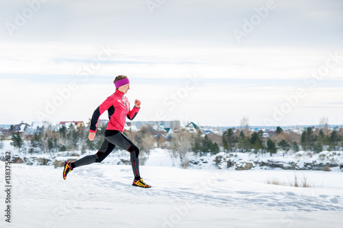 Winter running exercise. Runner jogging in snow. Young woman fitness model running in a city park.
