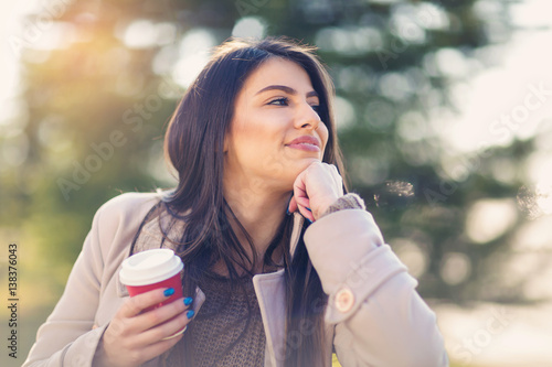 Portrait of a young woman laughing outside  holding coffee to go