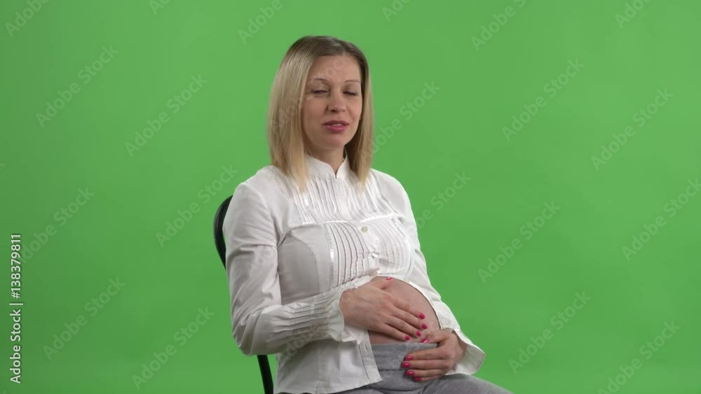 Pregnant woman sitting on a chair talking with some person against green screen Pregnant woman sitting on a chair talking with some person against green screen
