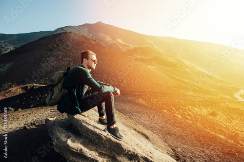 Man sitting on rock at sunrise on background of volcano Etna mountain in Sicily