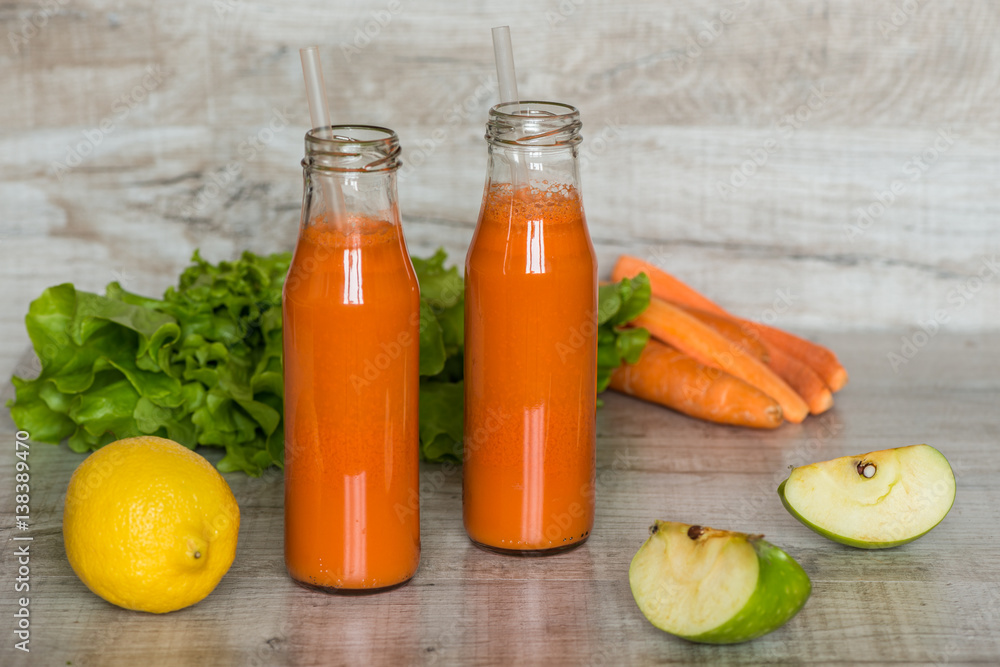 Fresh carrot juice in bottles on a grey wooden table Fresh carrot juice in bottles on a grey wooden table