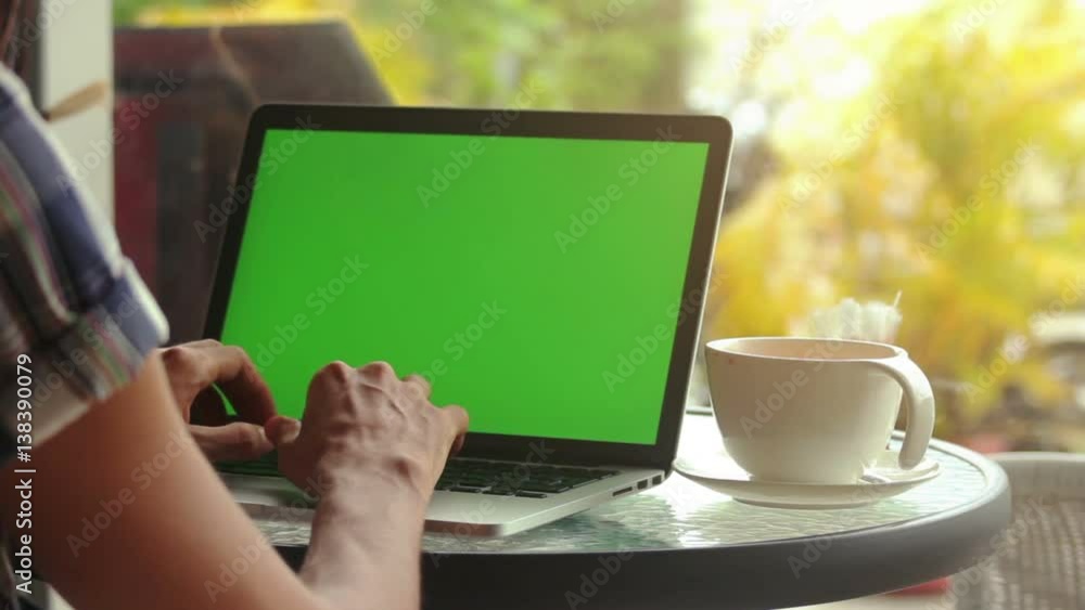 Close-up of male hands using laptop with green screen at cafe, man's hands typing on laptop keyboard in interior, side view of freelancer using computer in cafe Close-up of male hands using laptop with green screen at cafe, man's hands typing on laptop keyboard in interior, side view of freelancer using computer in cafe