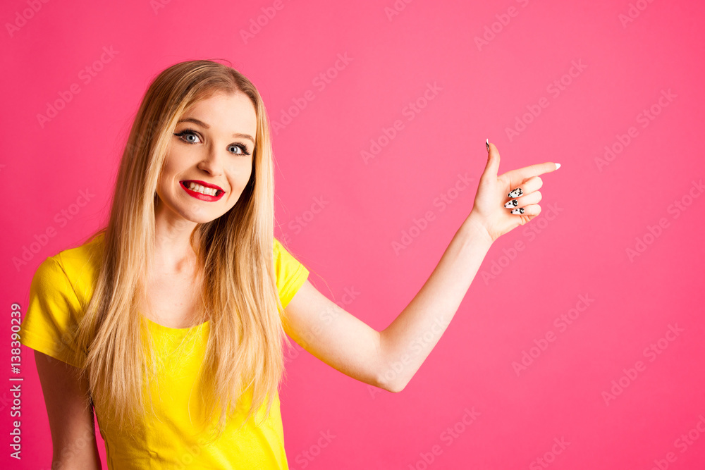 Cute young blonde teenage woman pose over pink background in vibrant yellow t shirt pointing in copy space as advertisement Cute young blonde teenage woman pose over pink background in vibrant yellow t shirt pointing in copy space as advertisement