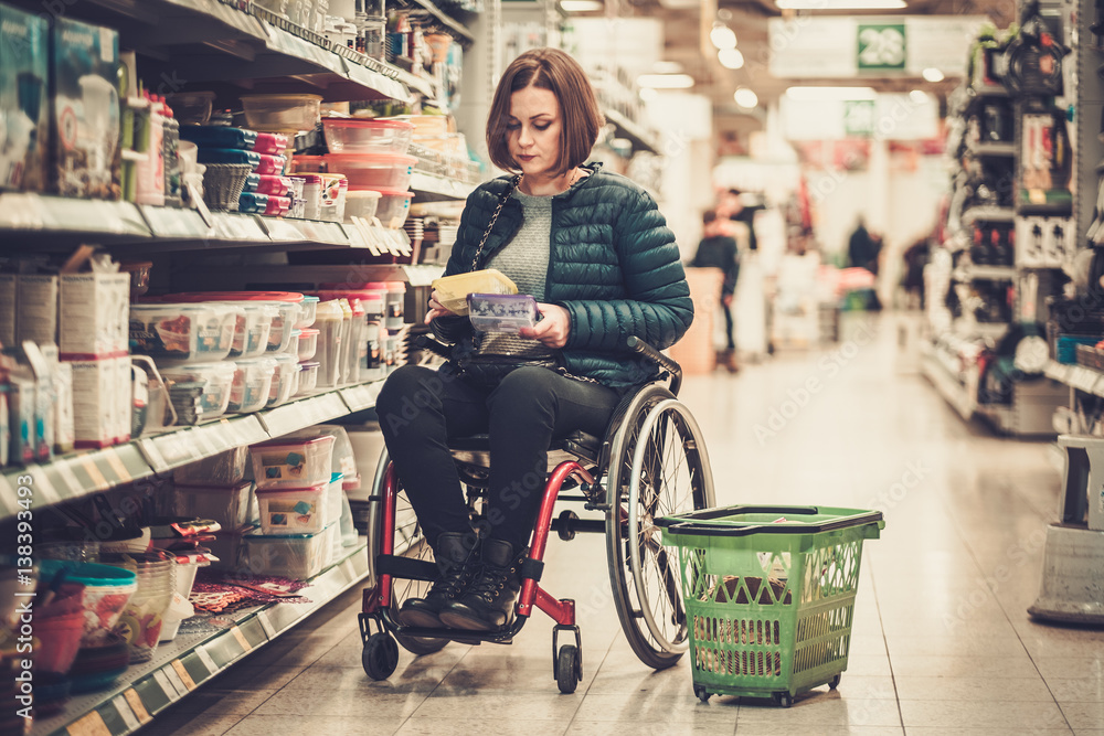 Disabled woman in a wheelchair in a department store - obrazy, fototapety, plakaty 