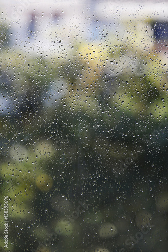 Rain splash drops on a window with green nature in background.