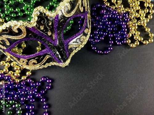 Mardi Gras mask and beads on a black surface 