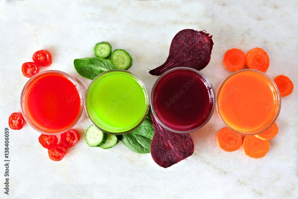Four types of juice with scattered vegetables, above view over a white marble background - obrazy, fototapety, plakaty 