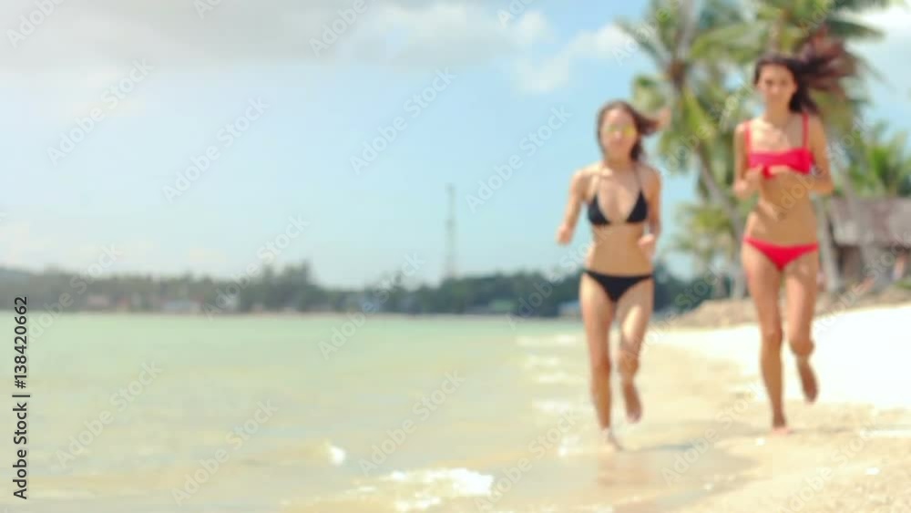 two beautiful models in bikinis running along the shore of a beach in slow motion two beautiful models in bikinis running along the shore of a beach in slow motion