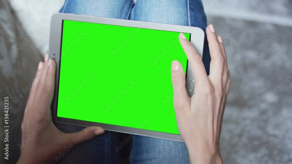 Young woman in blue jeans sitting on couch uses tablet pc with pre