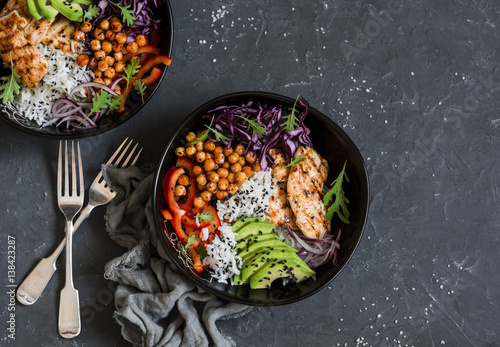 Grilled chicken, rice, spicy chickpeas, avocado, cabbage, pepper buddha bowl on dark background, top view. Delicious balanced food concept photo