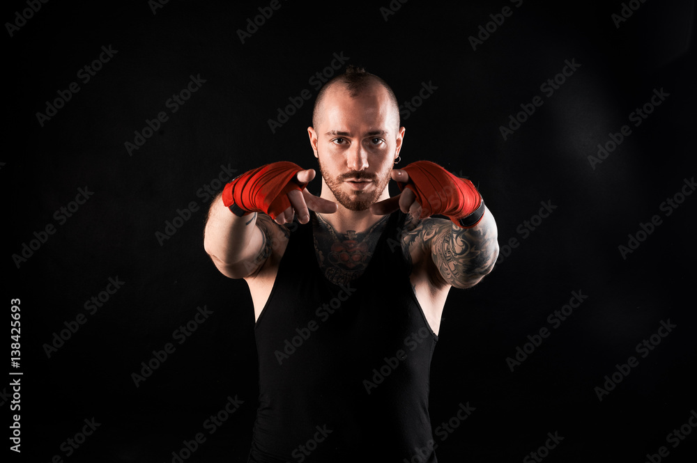 Fighter show into the camera. Bearded man with muscular body and tattoo in black t-shirt on dark background. Point concept.