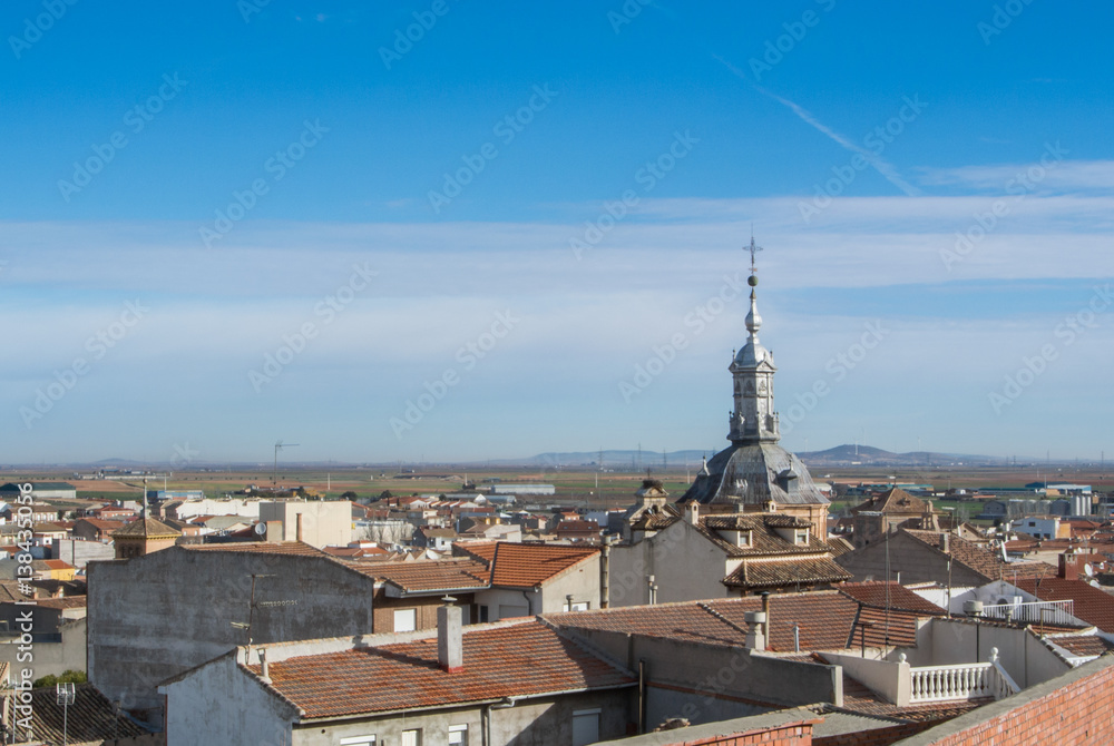 A panoramic view to spanish town Consuegra (Castilla-La Mancha) and a church over the orange tile roofs on sunny day.