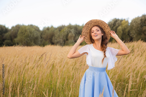 Tableau sur toile Girl with circlet of flowers walking in golden dried grass field