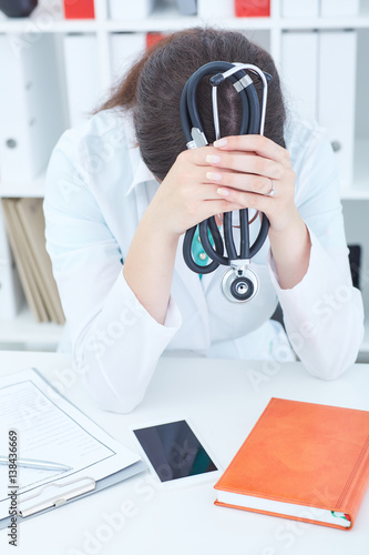 Stressed female medical doctor sitting at the desk in office.
