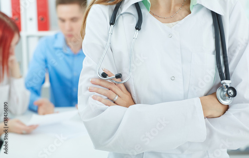 Female medicine doctors s hands crossed on her chest close up with family couple on the background. Medical help or insurance concept. Physician reception concept.