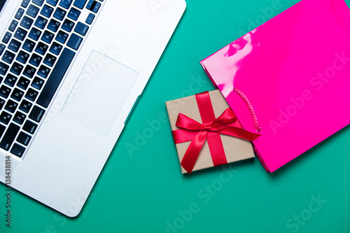 beautiful small gift, pink shopping bag and modern silver laptop on the wonderful blue background