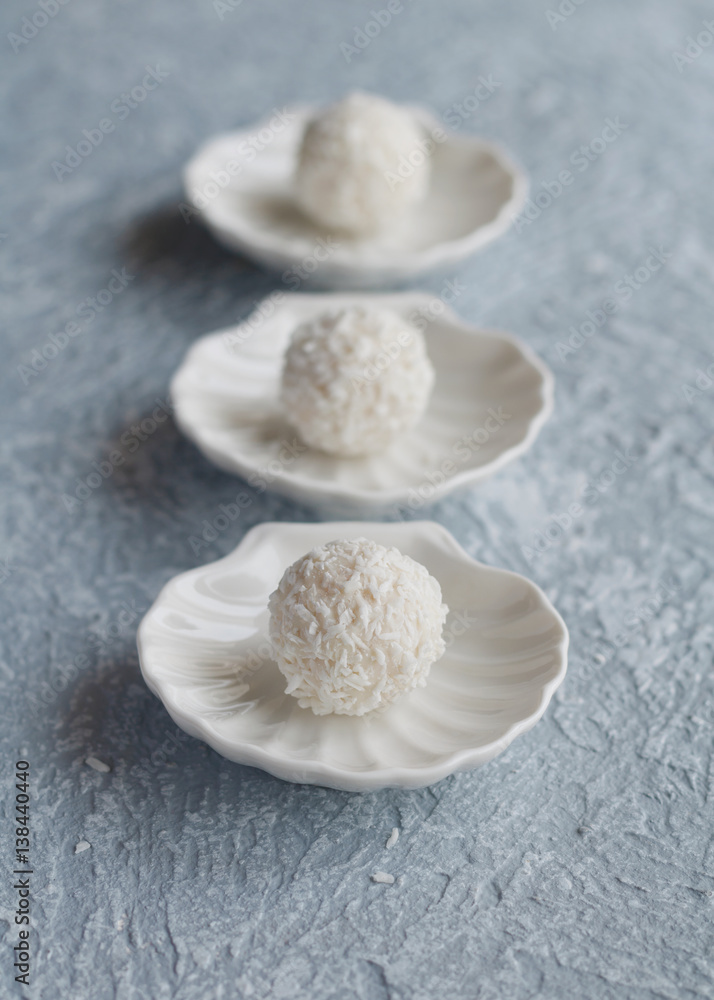 Close-up of white coconut candy in the shape of a ball on a white saucer in the form of shells on blue background.