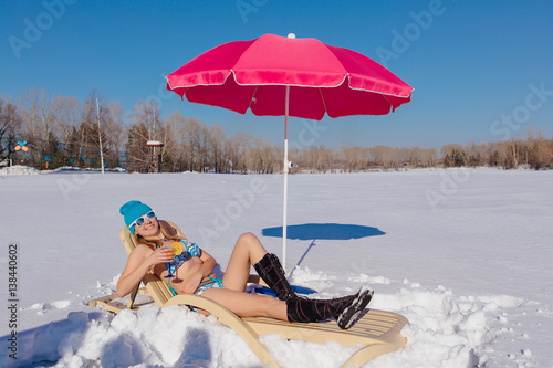 Beautiful girl relaxing on the sunbed on the winter snowy beach.