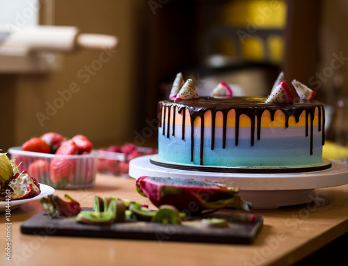 chocolate cake with multicolored shortcakes decorated by dragon fruit with Organic fresh kiwi fruit and half of dragon fruit on a wooden cutting board,red ripe strawberry in plastic box