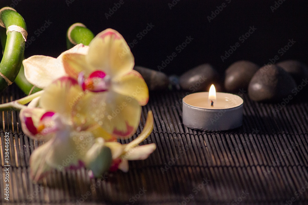 Gelbe Orchideen auf einer Bambusmatte mit Kerzen und schwarzen Steinen Gelbe Orchideen auf einer Bambusmatte mit Kerzen und schwarzen Steinen