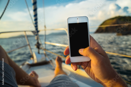 Rest on a yacht with a phone in hand. Summer leisure. Male lying on the deck and enjoy your smartphone. The guy doing the photo feet on the background seascape and yachts. © galaganov