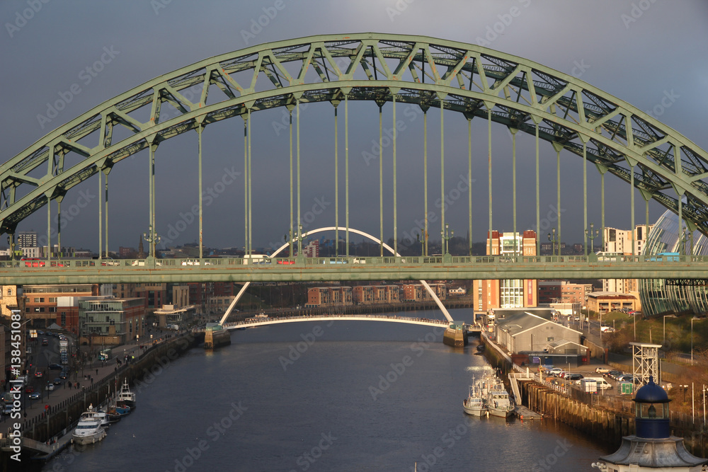 Dark storm clouds behind the Millennium and Tyne Bridges which are lit in a golden light by the sun breaking through the clouds