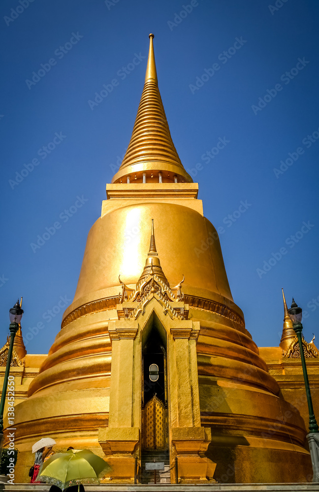 Tourists with umbrellas in front of the Golden Stupa in the Grand Palace in Bangkok