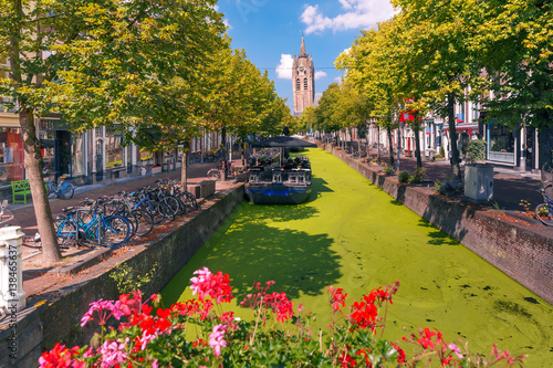 Schilderij op canvas The picturesque Oude Delft canal and leaning tower of Gothic Protestant Oude Kerk church on a sunny day in Delft, South Holland, Netherlands