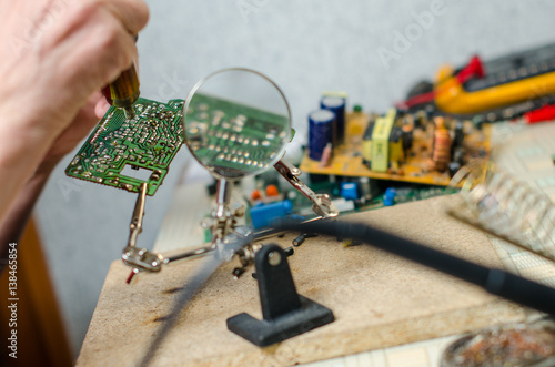 Engineer soldering microcircuit though magnifier. third hand