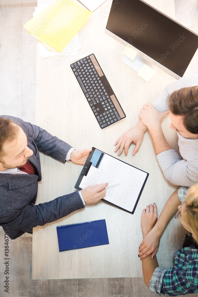 Top toned of salesman or manager offering agreement or contract for young couple. Man asking people to sign and to get credit card. Bank officer. Top toned of salesman or manager offering agreement or contract for young couple. Man asking people to sign and to get credit card. Bank officer.