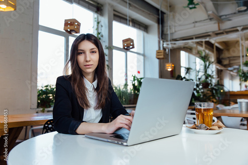 Young business woman sitting at table in cafe. Working with the notebook and glass of tea.