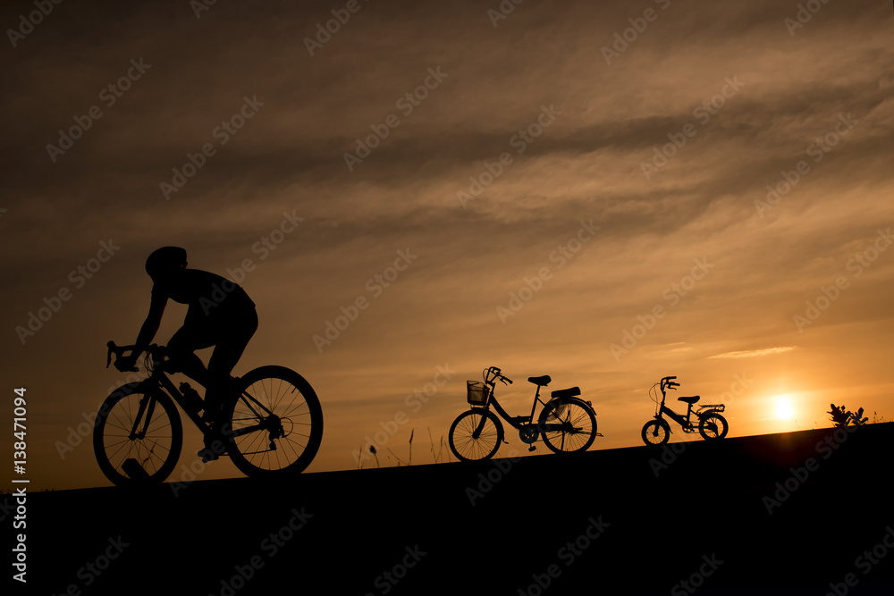 Fototapeta premium Silhouette of a cyclist and vintage bikes against sunset background in Thailand.