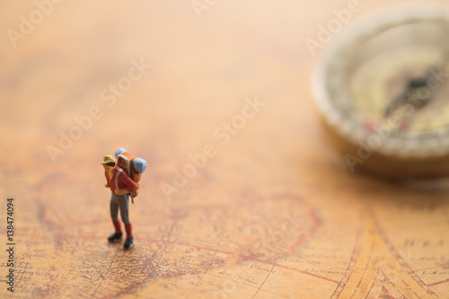 Miniature people : travellers standing on world map in front of vintage compass, exploring on earth background concept.