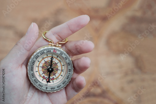 Golden compass in woman's hand with vintage world map background, travelling, exploring world concept