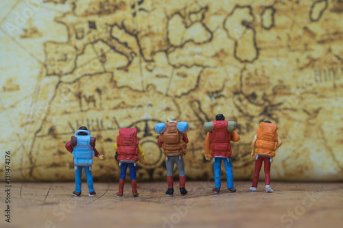 Miniature people: Group of traveler miniature mini figures with backpack standing and looking on vintage world map. Travelling concepts.