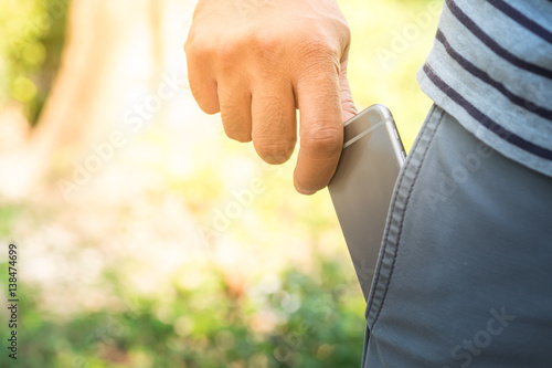 Asian man's hand picking smart phone from the front pocket of blue jeans