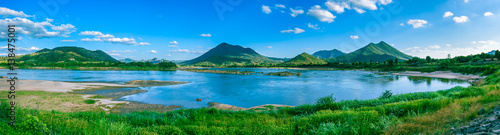 Panorama view of mountain full of green tree with river in front and clear blue sky.