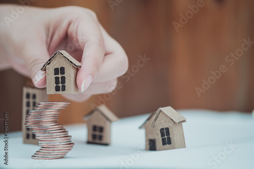 Woman's hand putting house model on coins stack. Concept for property ladder, mortgage and real estate investment .