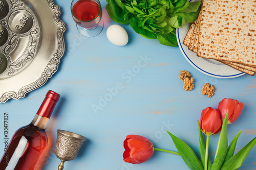 Passover holiday concept seder plate, matzoh, tulip flowers and wine bottle on wooden background. Top view from above