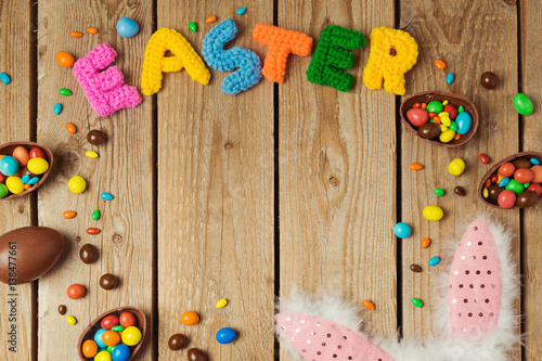 Easter holiday concept with chocolate eggs and bunny ears on wooden board background. Top view from above with copy space