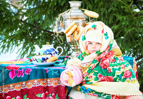 Baby girl in traditional national headscarf in the Russian samovar and bagles in the background.