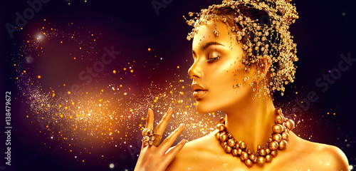 Gold woman skin. Beauty fashion model girl with golden makeup, hair and jewellery on black background