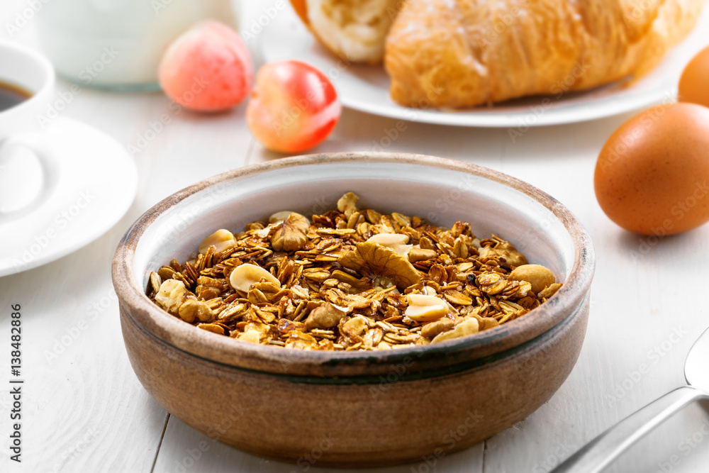 Healthy food for breakfast on a white wooden table. Oatmeal granola with nuts, coffee, croissants, eggs, milk and fruits for delicious healthy meal. Close-up. Healthy food for breakfast on a white wooden table. Oatmeal granola with nuts, coffee, croissants, eggs, milk and fruits for delicious healthy meal. Close-up.
