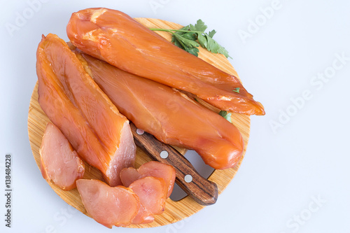 
Carpaccio.   Smoked chicken breast, whole and cut into thin slices, on a wooden cutting board on a light background.