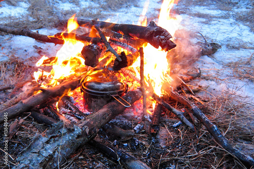 Pan on campfire at night in winter forest. Cooking in campaign camp fire. Travel accessories. Tourist rest.