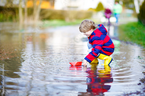 Fototapeta Naklejka Na Ścianę i Meble -  Little kid boy playing with paper ship by puddle