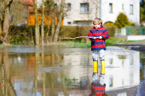 Little kid boy playing with fishing rod by puddle