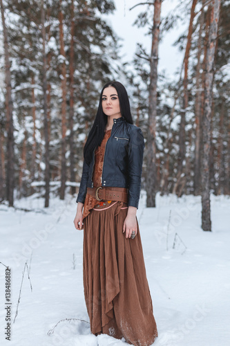 Girl in ethnic costume standing in winter forest, which is covered with snow