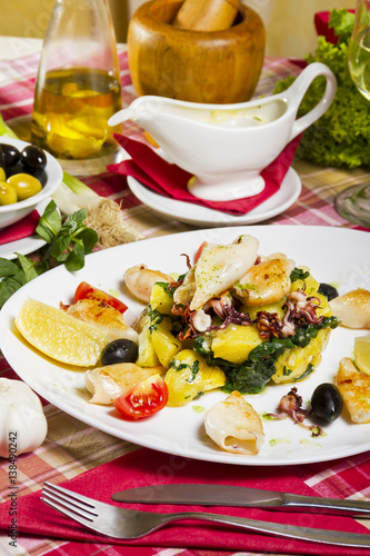 Grilled calamari on a white plate with boiled potatoes and chard  lemon  cherry tomatoes and olives.